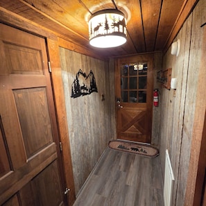 Un couloir intérieur en bois, avec une porte, un luminaire fixé au mur et un extincteur.