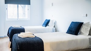 Quarto de hotel com duas camas, uma janela grande com persiana escura e uma parede branca com termostato.