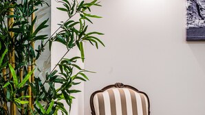 Quarto com piso de madeira, poltrona listrada, uma planta de bambu alta e um quadro na parede.