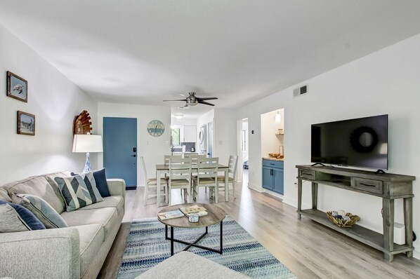 A modern living room with a sofa, coffee table, TV, and dining area.