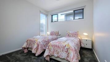 Un dormitorio con dos camas, un ventilador de techo, una ventana con persianas y una mesita de noche con lámpara.