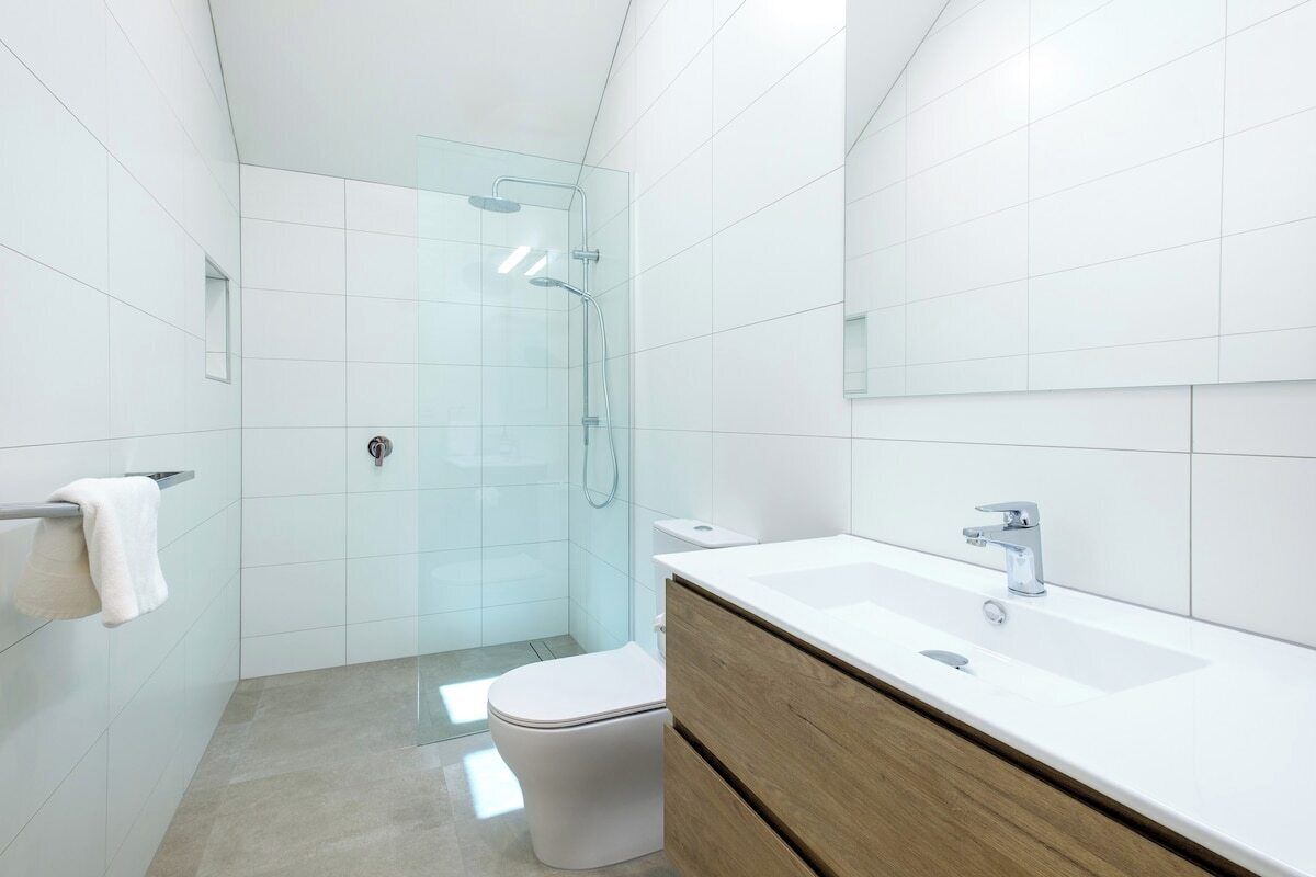 A modern bathroom with a glass shower enclosure, a white toilet, and a wooden vanity with a sink.