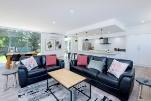 Un salon moderne avec un canapé en cuir noir, une table basse en bois et un coin repas comprenant une table et des chaises en bois.