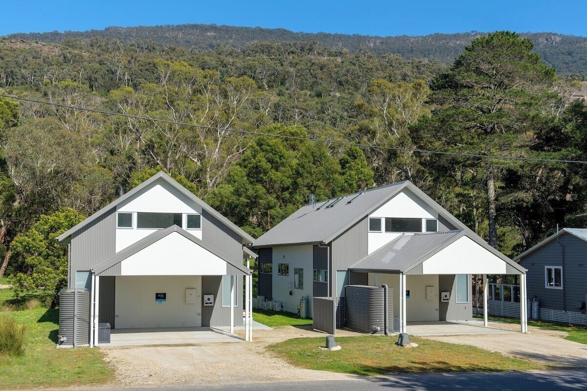 A row of modern, two-story buildings with attached garages, set against a backdrop of a hilly landscape with dense trees.