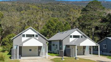 A row of modern, two-story buildings with attached garages, set against a backdrop of a hilly landscape with dense trees.