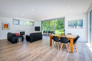A modern living room with a dining area, large windows, and a fireplace. - Serenity HG4: 4Br/3.5Ba with Absolute NP Frontage (Halls Gap)