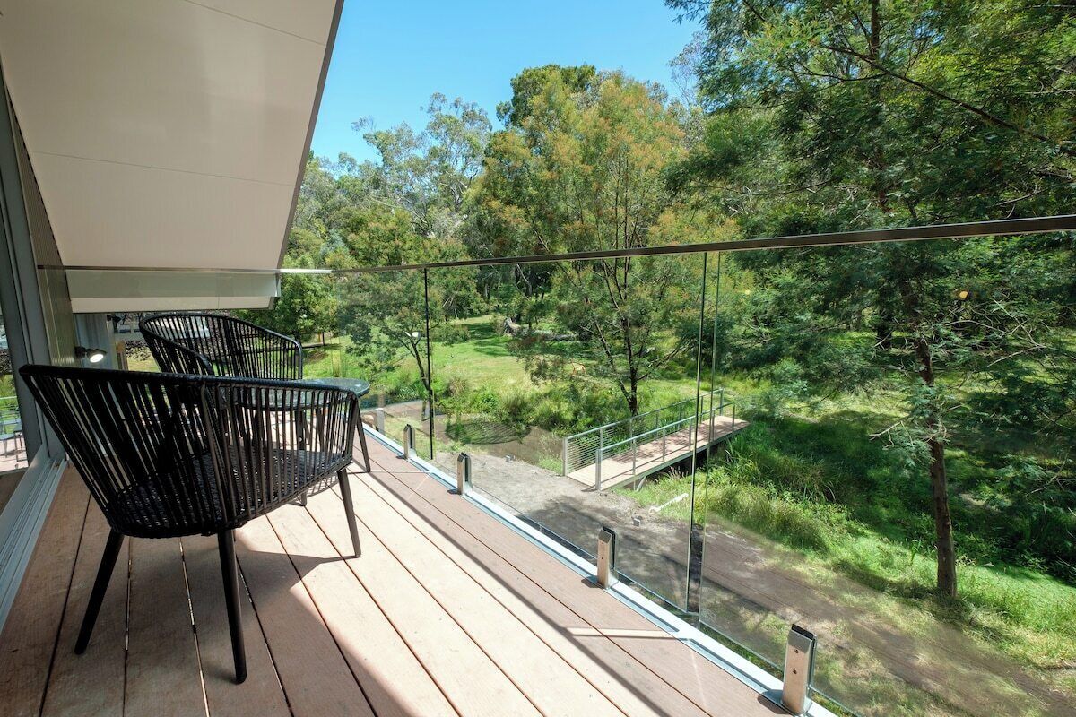 Ein Balkon mit Blick auf eine grüne Landschaft, einer Glasumlaufung und zwei schwarzen Stühlen.