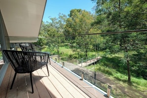 Un balcon donnant sur un paysage verdoyant, avec une balustrade en verre et deux chaises noires.