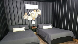 Une chambre avec deux lits, un climatiseur fixé au mur et une petite table avec une lampe.