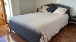 A neatly made bed with a grey headboard and a light-colored bedspread.