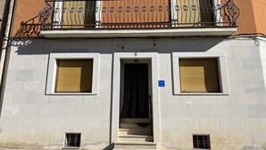 A building with a balcony, two windows with shutters, a door, and a blue sign.