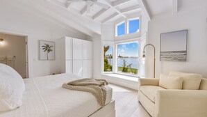 A bedroom with a large bed, a window with a view of the sea, and a white ceiling fan. - 4 Bed / 4 Bath with Stunning Views of Bimini Bay ! (Anna Maria)