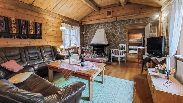Interior acogedor de una cabaña con pared de piedra, mobiliario de madera, chimenea y televisor.