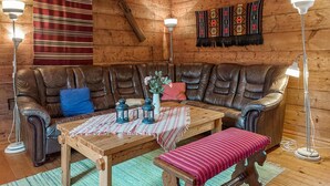 Interior acogedor de una cabaña de troncos con sofá de cuero, mesa de madera, banco y dos lámparas de pie.
