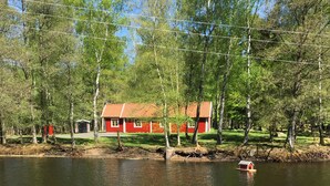 Una casa roja con techo de tejas junto a un lago, rodeada de árboles y una línea de electricidad sobre ella.