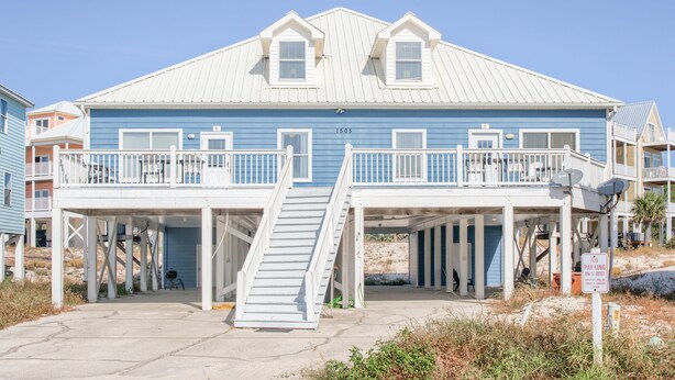 A beachfront house with a blue exterior, white railings, and a covered porch. - Dandy Sandy: Sleeps 24 - Pets - Pools - Hot Tubs (Gulf Shores)