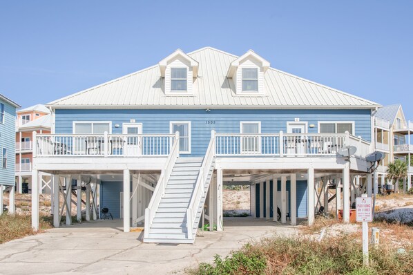A beachfront house with a blue exterior, white railings, and a covered porch.