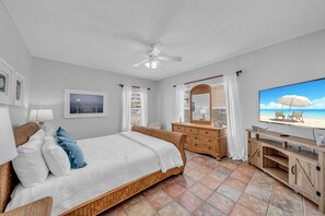 A bedroom with a bed, a dresser, a television, and a view of the beach.