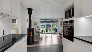 A modern kitchen with a central wood-burning stove, a built-in oven, and a dining area with a view to the outdoors. - Gorgeous apartment in Skagen with WiFi (Skagen)