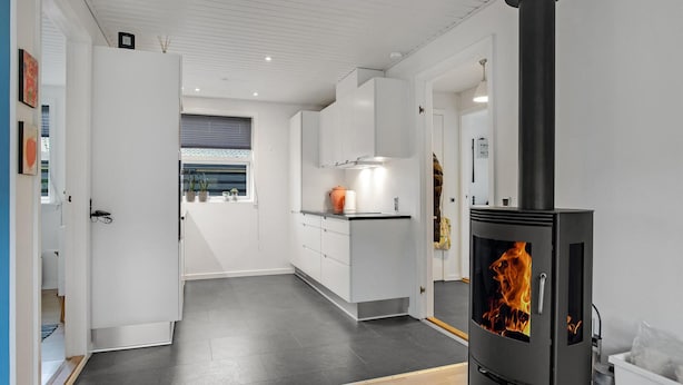 A modern kitchen with a central island, a black wood-burning stove, and a window with blinds. - Gorgeous apartment in Skagen with WiFi (Skagen)