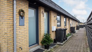 A row of brick buildings with numbered doors, a small potted plant, and black trash bins. - Gorgeous apartment in Skagen with WiFi (Skagen)
