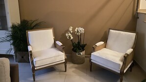 Two white armchairs with cushioned seats and wooden legs, positioned on a tiled floor against a beige wall. A wicker basket with white flowers is placed between them. - Townhouse 300 meters from the sea (València)