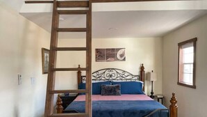 Une chambre à coucher avec un lit, une échelle en bois, une table de chevet, une lampe et une fenêtre.