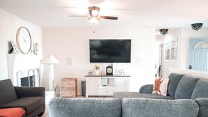 En stue med en grå sofa, et sort fjernsyn, en loftsvifte og et hvidt skab.