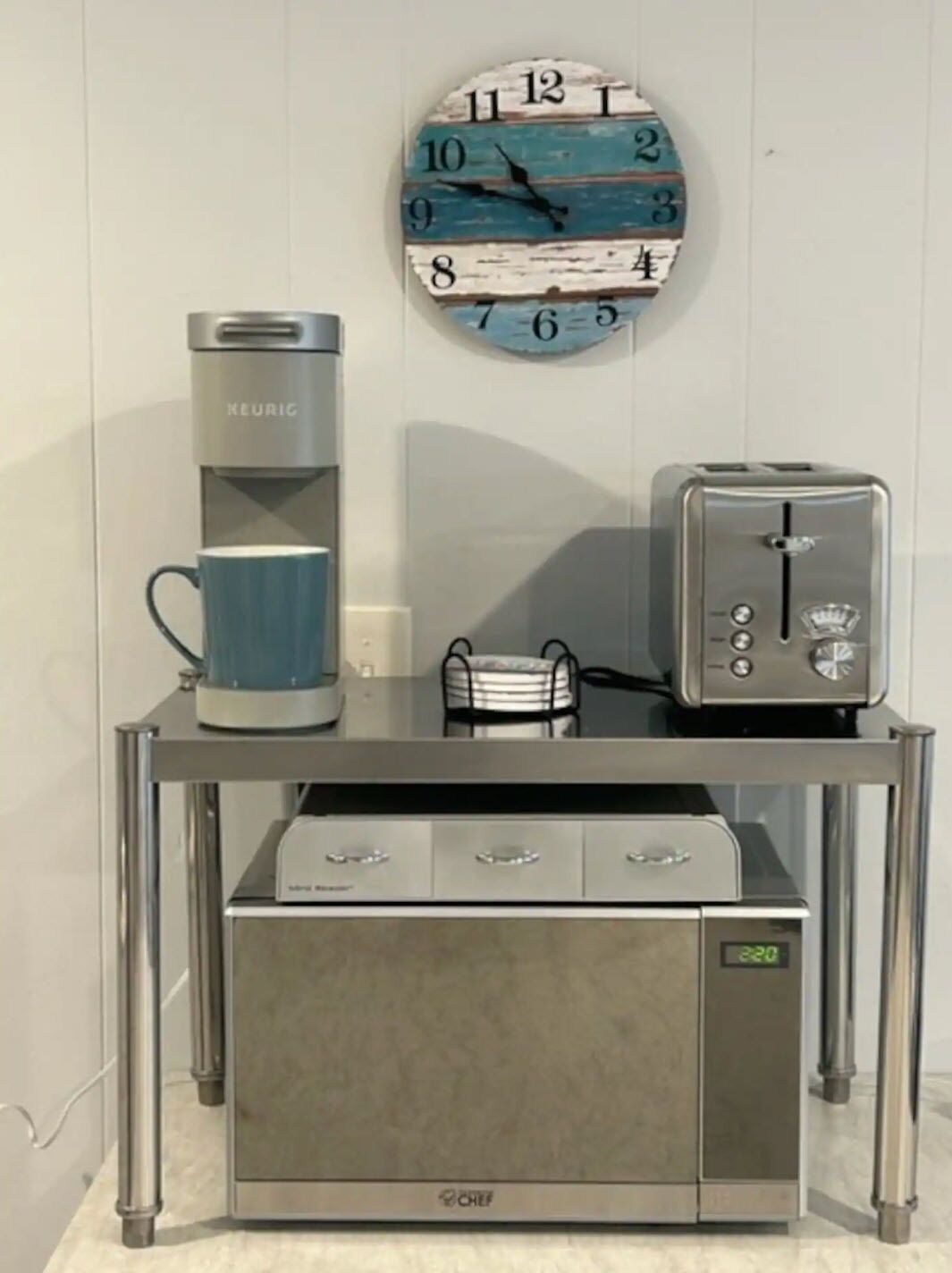 A kitchenette with a coffee maker, toaster, and a clock on the wall.