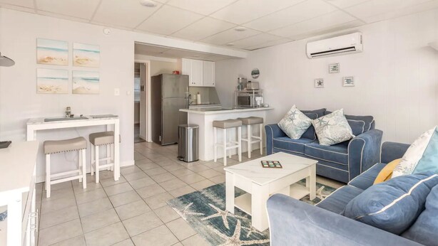A modern living room with a blue sofa, a white coffee table, and a kitchen area with a refrigerator and a microwave. - Clean, modern and well-equipped Ocean City condo (Ocean City)