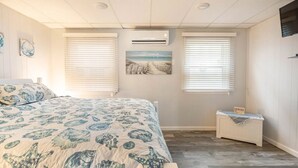 A bedroom with a bed, two windows with blinds, an air conditioner, a small bedside table, and a wall-mounted TV. - Clean, modern and well-equipped Ocean City condo (Ocean City)