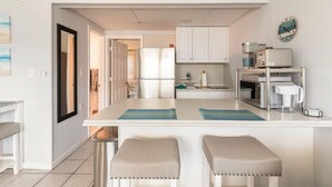 A modern kitchen with white cabinetry, a central island with stools, and a microwave on the countertop. - Clean, modern and well-equipped Ocean City condo (Ocean City)
