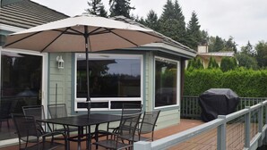 A covered patio with a table and chairs, a grill, and a view of the surrounding greenery. - Sunset Lake Retreat@ Lake Tapps-Lakefront, Spacious, Sports court, Kayaks (Lake Tapps)