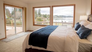 A bedroom with a large bed, two windows, a view of a lake, and a sliding glass door leading to an outdoor area. - Sunset Lake Retreat@ Lake Tapps-Lakefront, Spacious, Sports court, Kayaks (Lake Tapps)