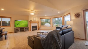 A living room with a fireplace, a television, a sofa, and large windows. - Sunset Lake Retreat@ Lake Tapps-Lakefront, Spacious, Sports court, Kayaks (Lake Tapps)