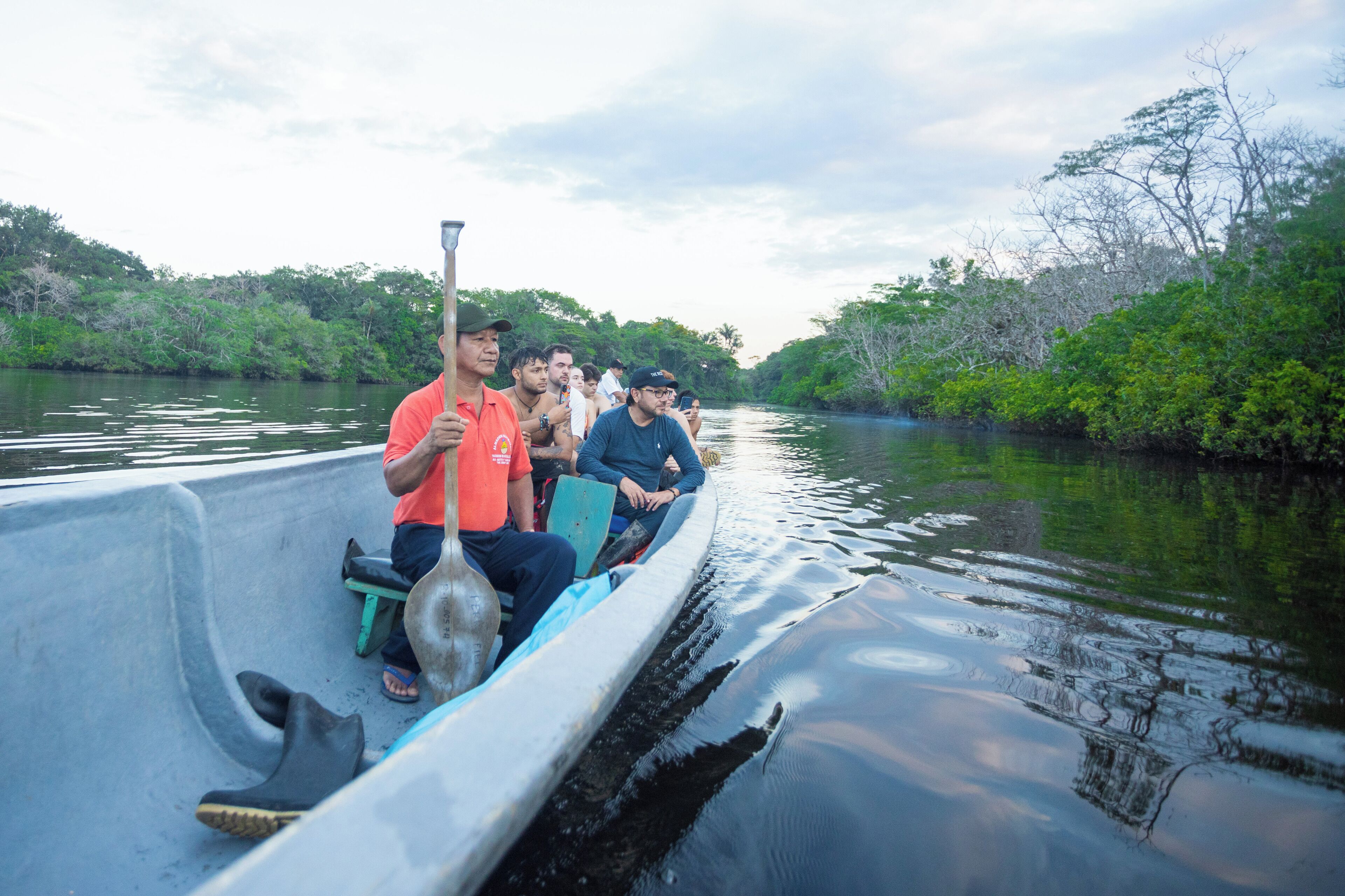 Un grupo de personas en un barco estrecho con un remo, rodeado de agua y vegetación.