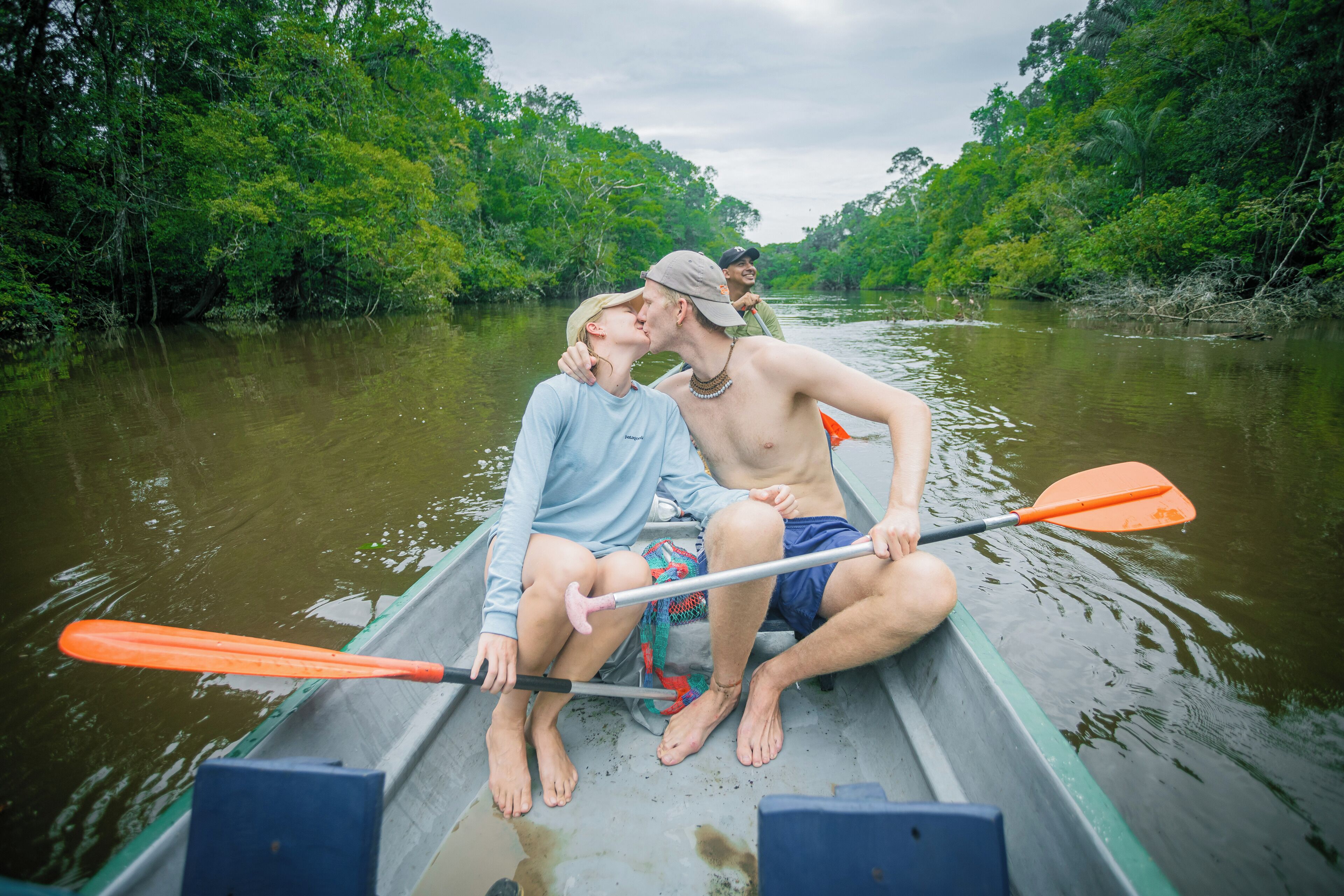 Two people in a narrow boat on a river surrounded by dense greenery.