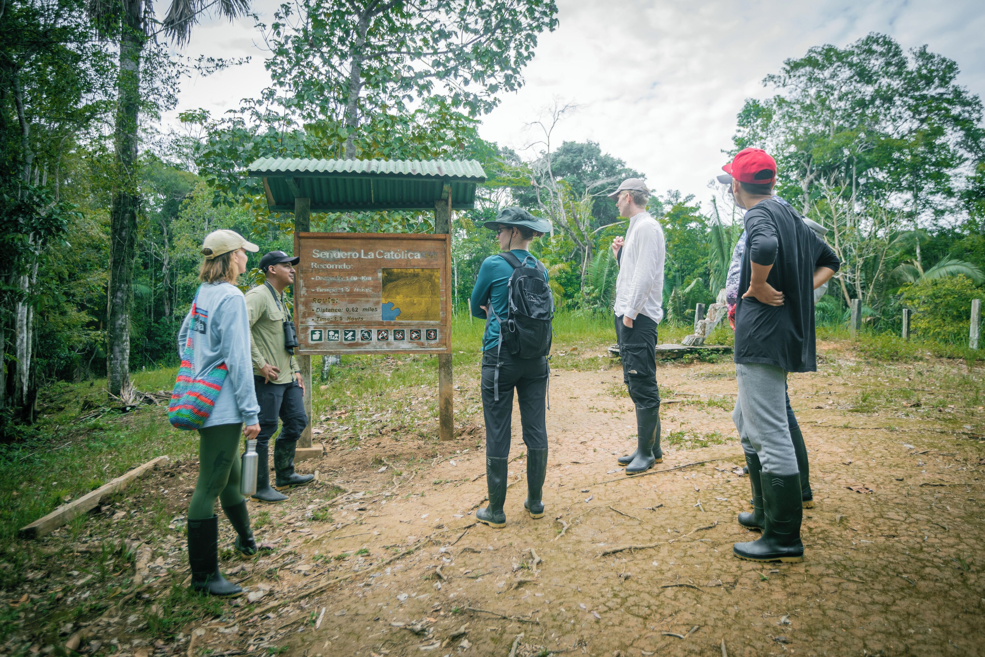 A group of people standing at a wooden signpost in a forested area.