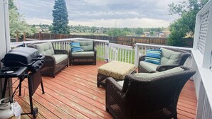 Eine überdachte Terrasse mit Korbmöbeln, einem Grill und Blick auf die Nachbarschaft.