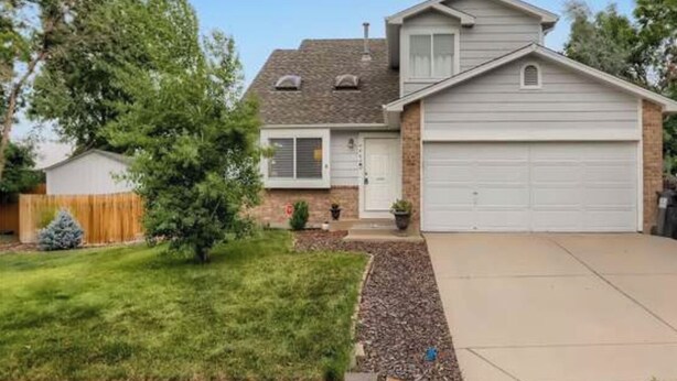 Ein eingeschossiges Haus mit Garage, einem kleinen Vorgarten mit Baum und einem Holzzaun.