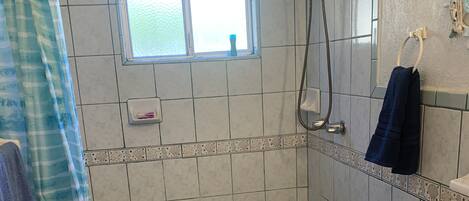 A bathroom with a shower, toilet, and a window.