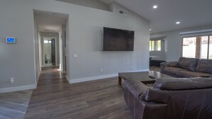 Un salon spacieux avec un grand canapé en cuir marron, un téléviseur à écran plat fixé au mur et un plancher en bois.