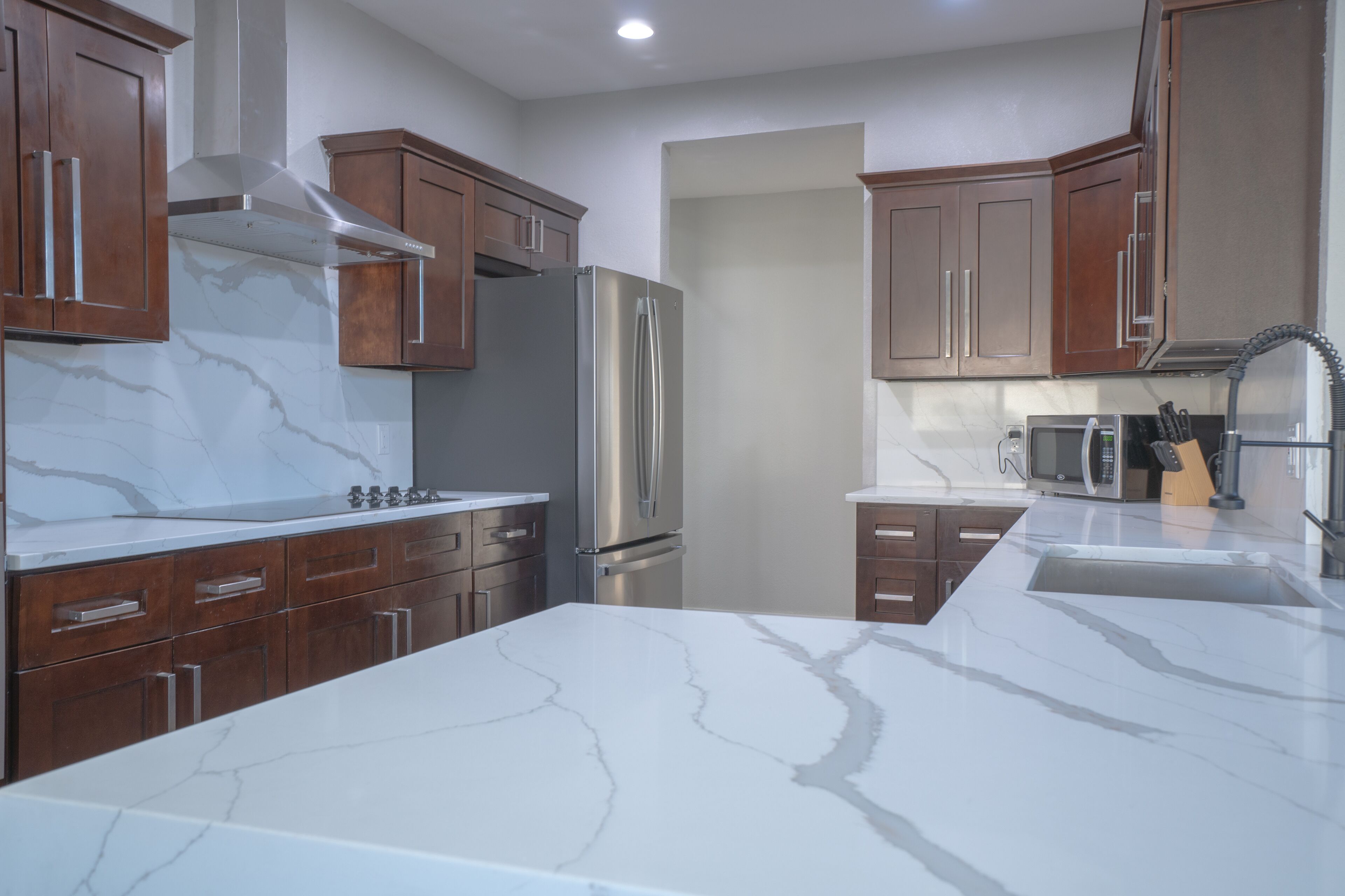 A modern kitchen with marble countertops, stainless steel appliances, and wooden cabinetry.