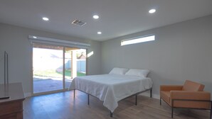 Une chambre à coucher comprenant un lit, une chaise, un bureau et une porte-fenêtre coulissante donnant sur un espace extérieur.