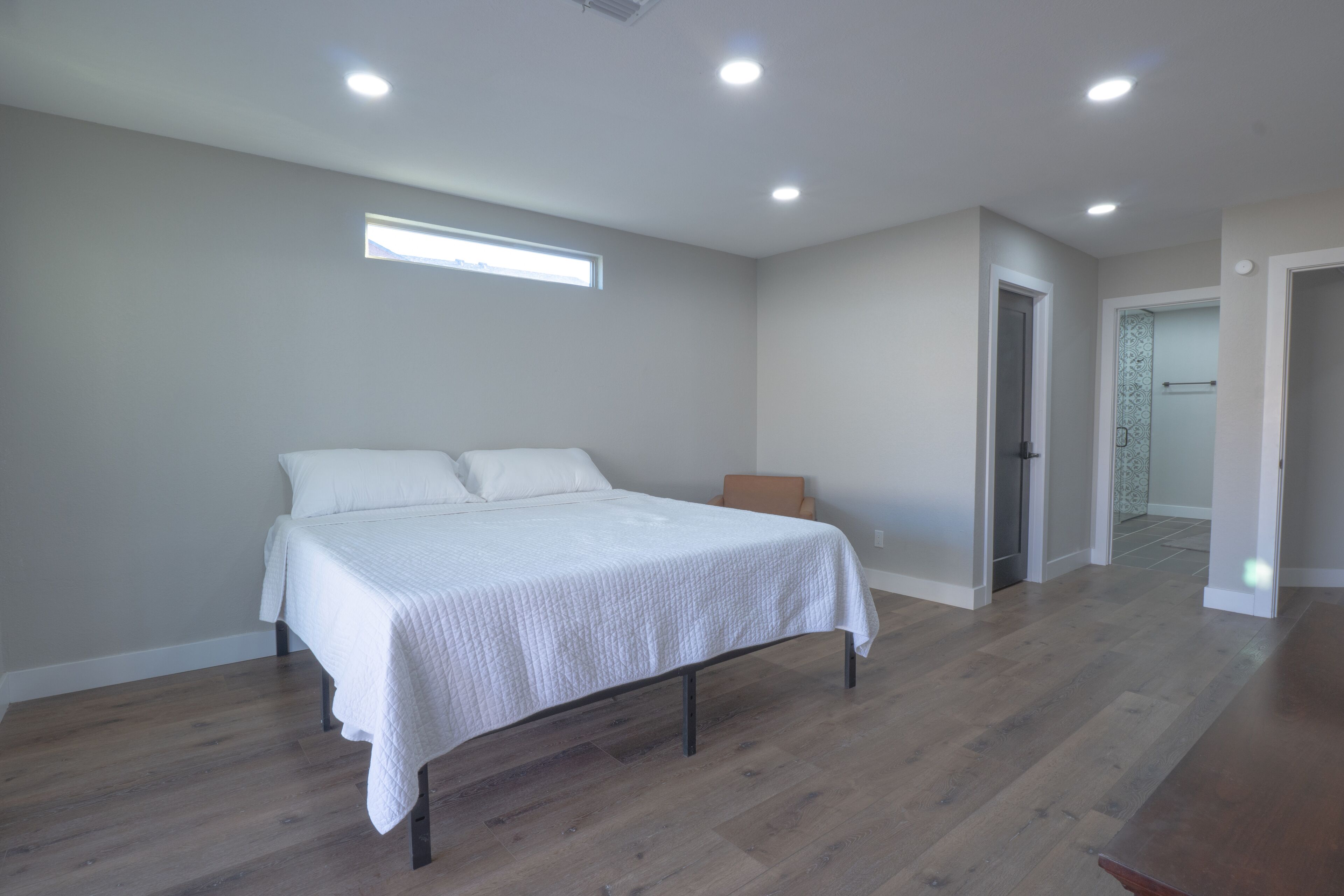 Un dormitorio con una cama, suelo de madera, una ventana y una puerta que da a otra habitación.