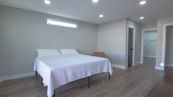 Un dormitorio con una cama, suelo de madera, una ventana y una puerta que da a otra habitación.