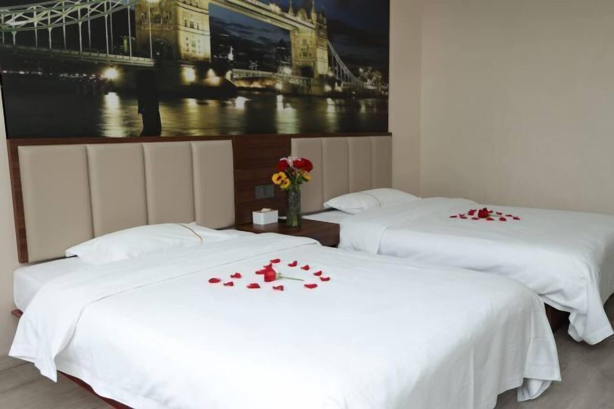 A hotel room with two beds, a nightstand with a vase of flowers, and a large wall mural of a bridge.