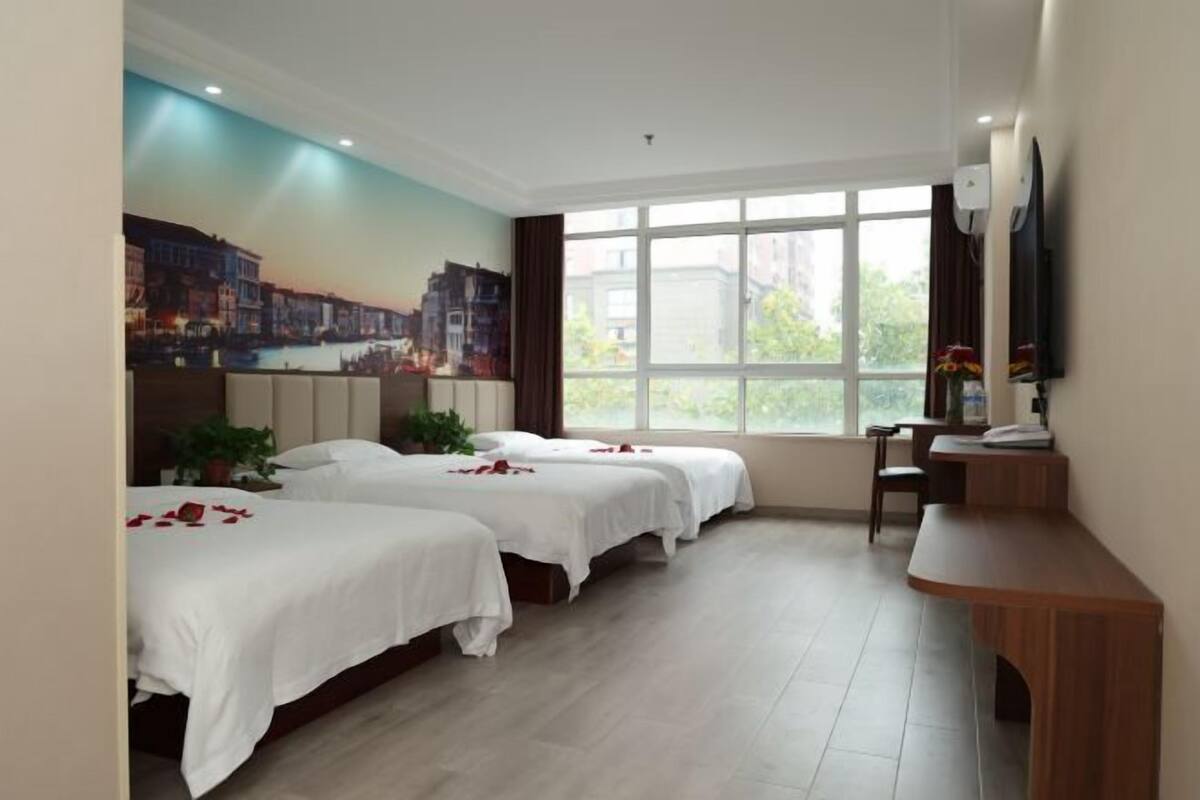 A hotel room with two beds, a desk, a TV, and a large window.
