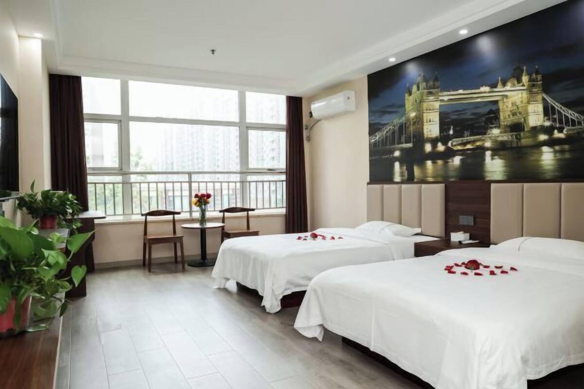 A hotel room with two beds, a large window with a view of a bridge, a dining area with a table and chairs, and a potted plant.
