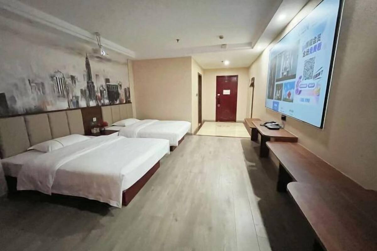 A hotel room with two beds, a wooden bench, a TV, and a cityscape mural on the wall.